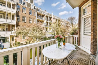 Masanın üzerinde çiçekli bir vazo ve sokağa açılan açık bir kapının yanında bir balkon.