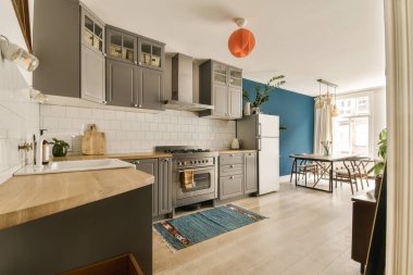 Mavi duvarları, ahşap döşemeleri ve duvarlarında beyaz fayanslar olan bir evde mutfak ve yemek odası.