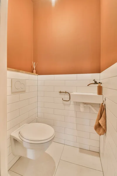 オレンジの壁と白いタイルの床を持つ小さなバスルームトイレはシャワーストールの前に配置されています — ストック写真