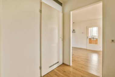 Ahşap zemini ve beyaz duvarları olan boş bir oda. Koridora açılan başka bir oda var.