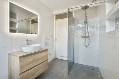 Lavabosu, aynası ve duş başlığı olan bir banyo duvarın yanında ahşap bir kibir var.