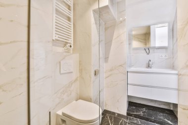 Mermer zemini ve beyaz duvarları olan modern bir banyo. Duş kabininde de tuvalet var. Lavabonun yanında.