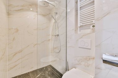 Beyaz mermer duvarları ve zemini olan bir banyo. Tuvaletin yanındaki duvara monte edilmiş bir duş başlığı da dahil.