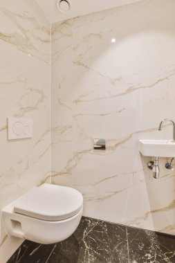 Mermer duvarları ve yerde siyah fayansları olan modern bir banyo. Köşesinde beyaz bir tuvalet var.