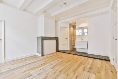 Odasında ahşap zemin ve beyaz duvarlar olan boş bir oturma odası pencereden gelen ışıkla aydınlanır.