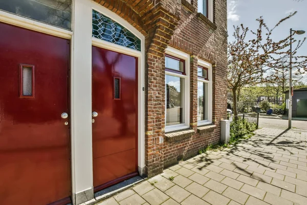 stock image a red door on the side of a brick building in an urban area with trees and bushes growing along it