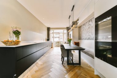 Odanın ortasında ahşap döşemeleri ve siyah dolapları olan modern bir mutfak yemek masası.