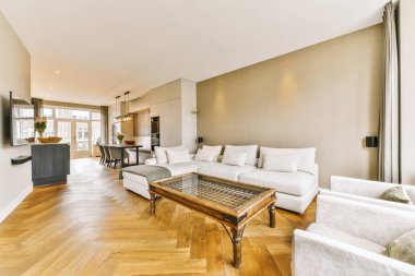 Odanın ortasında ahşap döşemeleri ve beyaz koltukları olan bir oturma odası açık bir mutfak alanıdır.