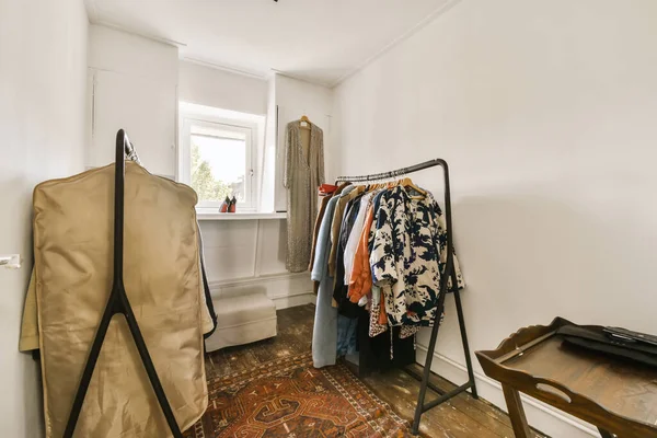 stock image a room with clothes hanging on hangers and an old chair in front of the window, next to it