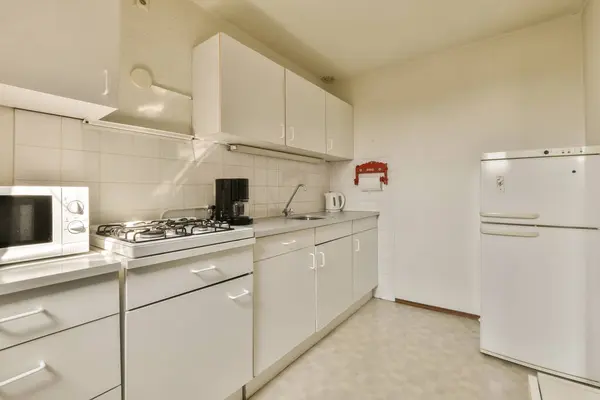 冷蔵庫 オーブン 電子レンジ 食器洗い機の前のカウンターの上に白いキャビネットと家電付きのキッチンエリア — ストック写真