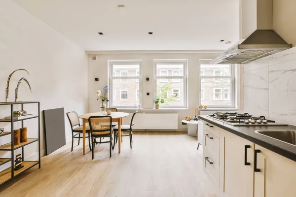 stock image a kitchen and dining area in a small apartment with white walls, wood flooring and marble countertops on either side