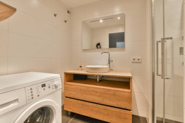 Köşesinde çamaşır makinesi ve kurutma makinesi olan bir çamaşır odası duvarında bir aynanın yanında.