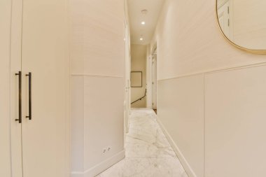 Her iki tarafında beyaz duvarlar ve mermer döşemeler olan uzun bir koridor, başka bir odaya açılan bir girişe açılıyor.