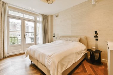 Tahta döşemeli bir yatak odası ve balkona açılan cam kapının önünde beyaz bir yatak odası.