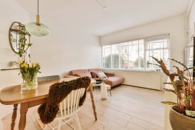 Ahşap zemin ve beyaz duvarları olan bir oturma odası. Etrafı saksı bitkileriyle çevrili ahşap bir yemek masası da dahil.