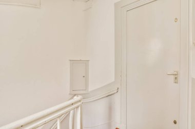 Beyaz duvarları ve ahşap zemini olan bir odanın içinde başka bir odaya açılan açık bir kapı var.