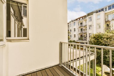 Arka planda ağaçlar ve binalar olan bir balkon, apartman penceresinden alınmış, Simn.
