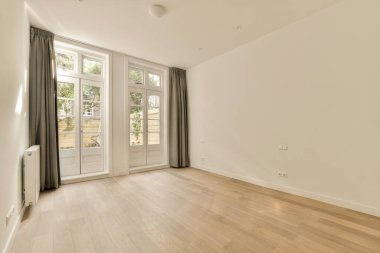 Boş bir oturma odası, ahşap döşeme ve arka bahçedeki bahçeye bakan büyük pencereler.