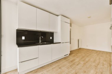 Apartmandaki beyaz dolapları ve siyah tezgahları olan boş bir mutfakta parke döşemeler var.