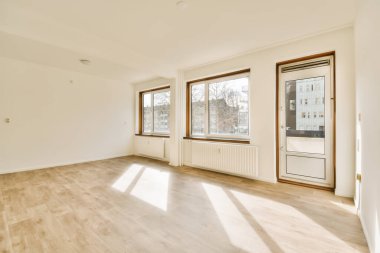 Boş bir oturma odası, ahşap döşeme ve evin önündeki sokağa bakan büyük pencereli.