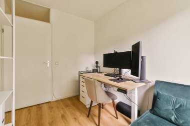 Masası, sandalyesi ve bilgisayar monitörü olan küçük bir oda arkasında dolaba açılan beyaz bir kapı var.