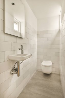 Duvarlarında beyaz fayanslar olan bir banyo ve lavabonun yanındaki tuvalet görünür.