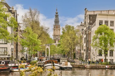 Nehrin diğer tarafındaki bazı tekneler ve kanalda yeşil ağaçların oluşturduğu binalar.