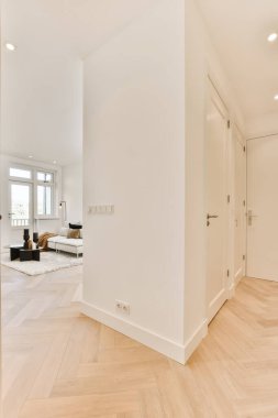 Odanın her iki tarafında tahta döşemeleri ve beyaz duvarları olan boş bir oturma odası, köşede bir kanepe var.