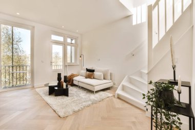 Odanın ortasında beyaz duvarları ve ahşap döşemeleri olan bir oturma odası var.