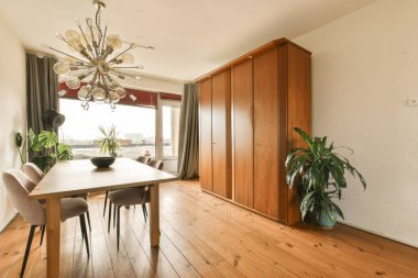 Ahşap zemin, beyaz duvarlar ve sokağa bakan büyük pencereli bir odada bir yemek masası ve sandalyeler.