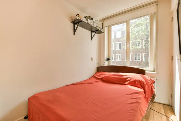 ヘッドボードに赤いベッドカバーが付いたベッドルームと部屋の窓は明るい白です — ストック写真