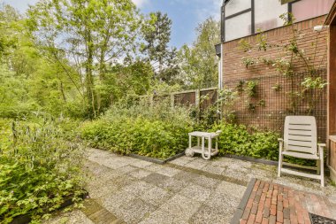 Duvarları tuğlalı ve yanında yeşil bitkiler olan arka planda kırmızı tuğlalarla çevrili bir avlu.