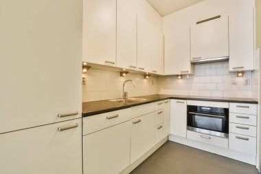 Beyaz dolapları ve siyah tezgahları olan bir mutfak fırının önündeki tezgahlar, lavabo ve bulaşık makinesi.