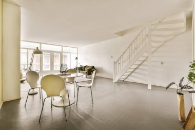 İkinci kata çıkan merdivenleri ve sandalyeleri olan bir oturma odası beyaza boyanmış bir dairede.