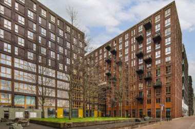 Caddenin kenarındaki çok eski binaların önünde arabalar park edilmiş ve insanlar sokakta yürüyor.