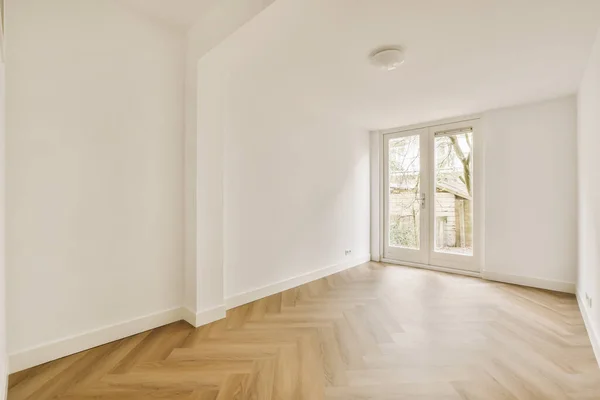 右側に白い壁と木の床がある空の部屋左側に大きな窓があります — ストック写真