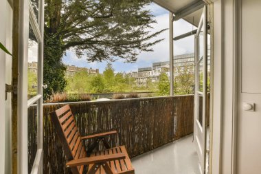 Ön tarafında bir bank ve ağaç olan bir dış alan. Görüntü içeriden alınıyor ama kimse onu göremiyor.