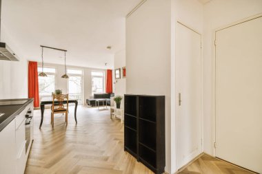 Ahşap zemin, beyaz duvarlar ve sobanın üzerinde siyah aletler olan bir dairede mutfak ve yemek odası.