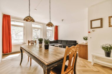 Ahşap döşemeli ve tavandan sarkan kırmızı perdeli bir yemek odası kanepenin yanında.