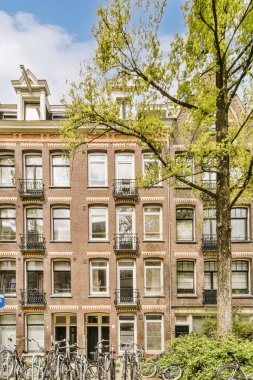 Caddenin her iki tarafında da birçok pencere ve balya bulunan bir apartmanın önüne parketmiş bisikletler, Amsterdam, Hollanda