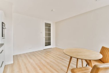 Beyaz duvarları ve ahşap döşemeleri olan boş bir oturma odası. Odanın ortasında yuvarlak bir yemek masası da dahil.