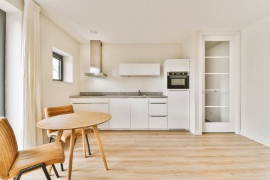 Beyaz duvarları, ahşap döşemeleri ve verandaya açılan açık kapısı olan bir odada mutfak ve yemek odası.