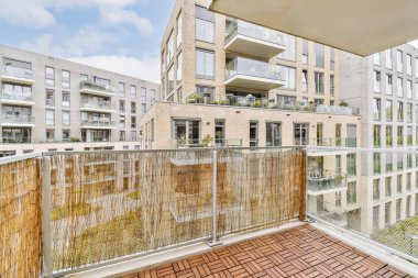 Arka planda bazı bitkiler ve binalar olan bir balkon, bir apartmandan görüldüğü gibi.