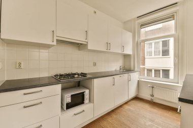 Ocağın, fırının ve bulaşık makinesinin önündeki adada beyaz dolapları ve siyah tezgahları olan bir mutfak.