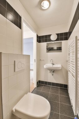 Duvarlarında siyah beyaz fayanslar olan küçük bir banyo, tuvalet ve lavabo yukarıdan çekilen bu resimde görülebilir.