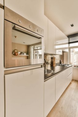 Odanın ortasında beyaz dolaplı ve siyah tezgahlı bir mutfak duvarda büyük bir ayna var.