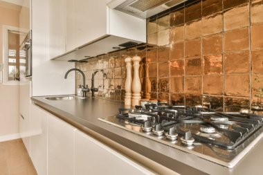 Duvarında bakır kiremitler olan bir mutfak ve odanın ortasında yemek pişirmek için kullanılan ocaklar.