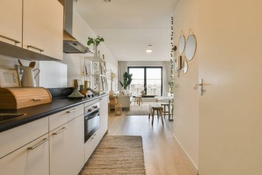 Yerde beyaz dolapları ve siyah tezgahları olan uzun, dar bir mutfak.