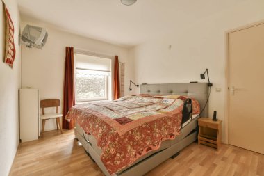 Yatağın üzerinde ahşap döşemeli ve kırmızı çarşaflı bir yatak, pencerenin yanında.