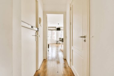 Beyaz duvarları ve yan yana ahşap döşemeleri olan uzun bir koridor, oturma odasına çıkıyor.